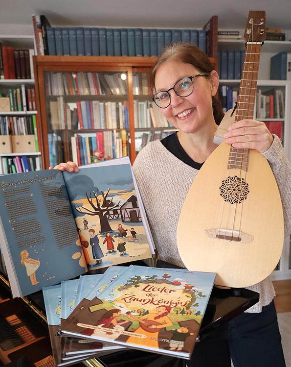 Christine Hinrichs mit den druckfrischen Bilderbüchern und ihrer Mogellaute  einer Ukulele in Lautenform. 